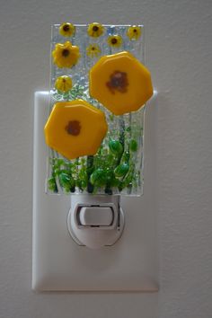 two yellow flowers are placed on a white light switch cover with green leaves and daisies