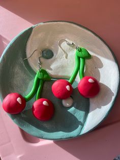 two green and red earrings sitting on top of a white plate next to a pink wall