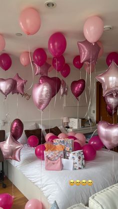 pink and silver balloons are floating in the air above a bed with white sheets on it