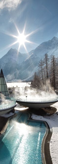 the sun shines brightly over an outdoor swimming pool with snow and mountains in the background