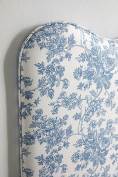 an upholstered headboard with blue and white floral print on it, against a white wall