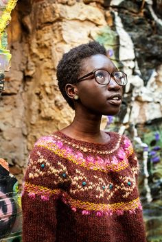 a woman with glasses standing in front of a rock wall and looking off into the distance