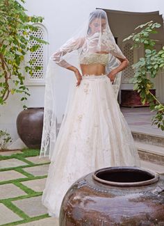 Elevate your style with the stunning Ivory Floral Embroidered Lehenga Set, a breathtaking blend of traditional elegance and modern sophistication. Crafted from luxurious organza, this ivory lehenga is layered with soft silk and French lace, creating a rich, textured base. Intricate tone-on-tone threadwork and zardosi embroidery enhance the fabric, while hundreds of shimmering, hand-cut organza flowers are scattered throughout, adding a whimsical, ethereal charm. The waistline, adorned with delicate floss embroidery and hand-appliquéd beads, exudes opulence and grace. Paired with a strapless crop blouse, featuring sparkling beads and intricately hand-cut organza flowers. With peek-a-boo lace details and an underlayer of fine French lace and silk, the blouse is both romantic and contemporary Strapless Blouse Lehenga, Ivory Lehenga, Strapless Blouse, Blouse Lehenga, Zardosi Embroidery, Organza Flowers, Embroidered Lehenga, Indian Wedding Wear, Indian Outfit