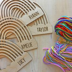 wooden name tags with rainbows on them and yarn next to eachother that says, ryan, taylorie, ayelor, lucy