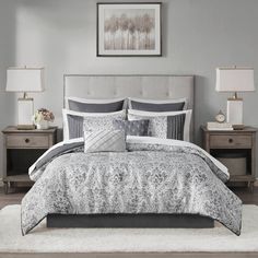 a bed with grey and white comforter in a bedroom next to two nightstands