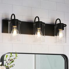 a bathroom light with three lights on the wall next to a mirror and flower vase