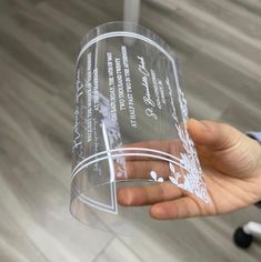 a person holding up a clear plastic cup with writing on the side and flowers in it