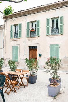 an outdoor table and chairs in front of a building with green shutters on the windows