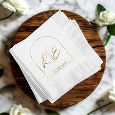 napkins with gold foil on them sitting on a wooden plate next to white flowers