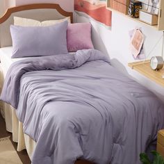 a bed with purple sheets and pillows in a small room next to a wooden shelf