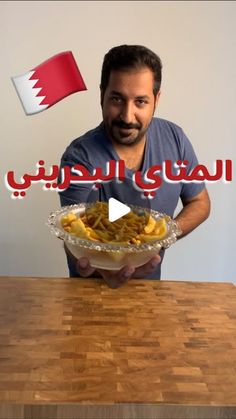 a man holding a bowl filled with food on top of a wooden table next to a flag