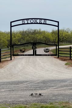 a gated entrance to a dirt road with trees in the background and a sign that says stocker on it