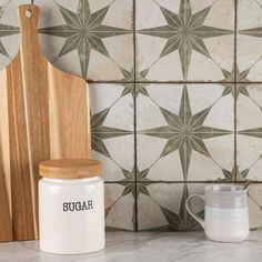 a wooden cutting board sitting on top of a counter next to a ceramic wall tile