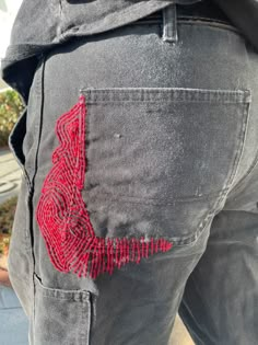 the back pocket of a pair of jeans with red threadwork on it, and a man's hand in his pocket