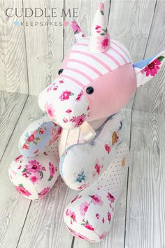 a pink and white stuffed animal with flowers on it's head sitting on a wooden floor