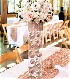 a tall vase filled with white flowers on top of a wooden table covered in glitter