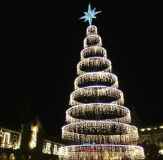 a lit christmas tree in front of a building at night with lights on the top