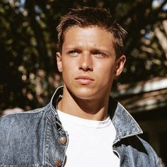 a young man wearing a denim jacket and white t - shirt looking at the camera