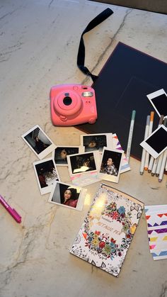 a table topped with pictures and pens next to a camera on top of a counter