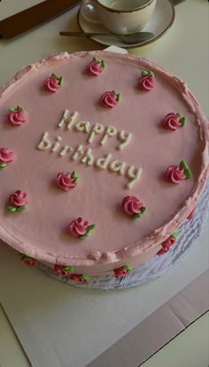 a birthday cake with pink frosting and roses on it, sitting on a table