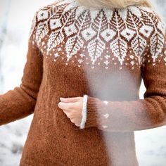 a woman wearing a brown and white sweater is standing in the snow with her hand on her hip