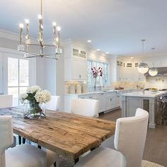 an open concept kitchen and dining room with white chairs, wood table, chandelier