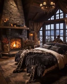 a bedroom with a stone fireplace and large windows overlooking the mountains is furnished with luxurious bedding