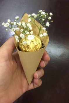 a hand holding a paper cone filled with white flowers and chocolate covered in gold foil