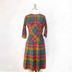 !950's brightly colored wool plaid fit and flare dress in orange, gold, green and black. Fitted at the waist, the bias skirt starts low. It has 3/4 raglan sleeves, a side zipper and 3 covered buttons at the back. There are two breastpockets. It is unlined and has raglan sleeves. Great autumn dress! Fits up to a current size 2 Measurements with room for comfort: Bust up to: 31 inches. Waist up to: 26 inches Hips up to: 37 inches Exact measurements taken flat to compare to a garment which fits wel Fitted Plaid Retro Vintage Dress, Fitted Retro Plaid Vintage Dress, Retro Plaid Fitted Vintage Dress, Fitted Retro Plaid Dress For Fall, Vintage A-line Plaid Dress, Retro Plaid Mini Dress, Vintage Plaid Dress For Fall, Vintage Plaid A-line Dress, Fitted Plaid Vintage Dress