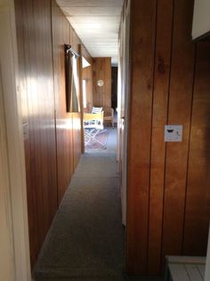 an empty hallway with wood paneling on the walls and carpeted floor, leading to another room