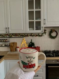 someone is holding up a coffee mug in their kitchen with christmas decorations on the counter