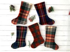 four plaid christmas stockings hanging on a white wooden wall with holly and pineconis