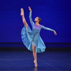 a woman in a blue dress is doing a ballet move on stage with her arms outstretched