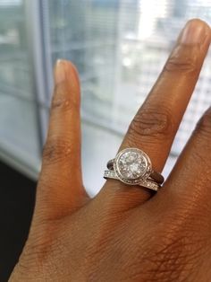 a woman's hand with a diamond ring on top of her finger in front of a window