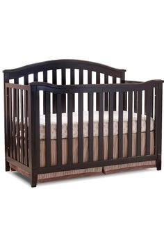 a baby crib with white sheets and brown wood trimmings on the sides