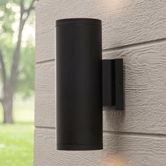 a black outdoor light mounted on the side of a building with trees in the background