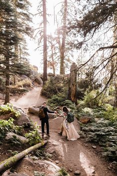 a bride and groom walking down a trail in the woods holding each other's hands