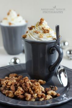 two cups filled with whipped cream and walnuts on top of a black saucer