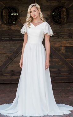 a woman standing in front of a wooden door wearing a white dress with ruffled sleeves