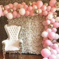 a chair sitting in front of a wall with balloons on it and a balloon arch