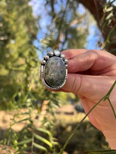 This moss agate gemstone inspired the Everglades Ring design.  The agate features green plumes that create depth and dimension at every angle. The ring also features a mother of pearl and 6 hand formed silver ball elements.  The ring features a straight ring shank in a size 8.  The ring will be packaged in a black gift box perfect for storing or gifting! Bohemian Moss Agate Gemstone Jewelry, Handmade Silver Rings With Moss Agate, Handmade Silver Moss Agate Rings, Handmade Silver Jasper Rings, Handmade Oval Moss Agate Ring, Distinctive Green Jasper Jewelry, Moss Agate Ring With Natural Stones, Bohemian Agate Ring With Large Stone, Silver Moss Agate Ring With Natural Inclusions