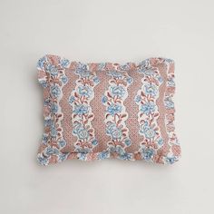 a pink and blue floral pillow on a white wall with a light brown back ground