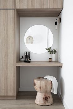 a wooden stool sitting under a round mirror on top of a shelf next to a white wall