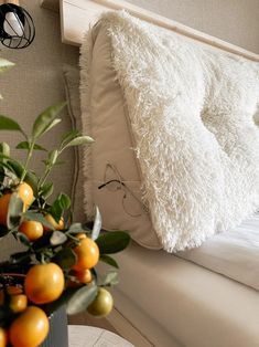 a bed with white pillows and oranges on top of it next to a potted plant