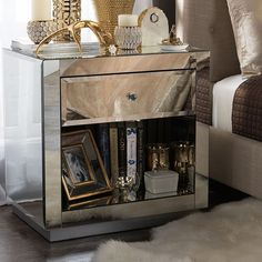 a mirrored side table with pictures, candles and other decorative items on it next to a bed