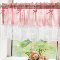 a vase with flowers sitting on a window sill in front of a checkered valance