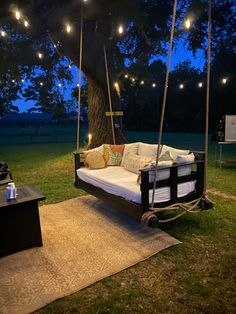 an outdoor swing bed with lights hanging from it's sides and pillows on the ground