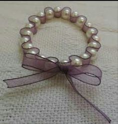 a close up of a bracelet with pearls and ribbon on a white tablecloth background