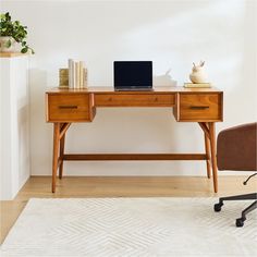 a wooden desk with a laptop on top of it next to a chair and potted plant