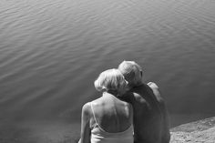 two people sitting on the edge of a body of water with their backs to each other